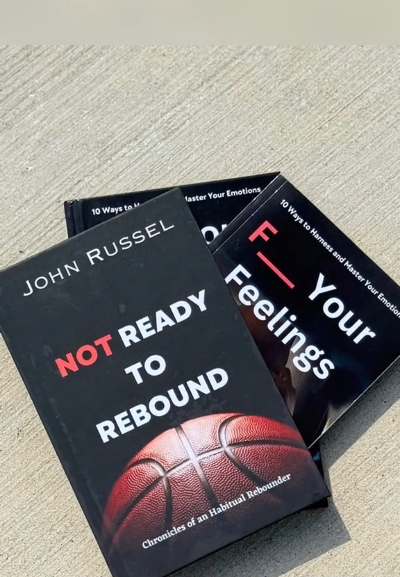Copies of John Russel books Not Ready to Rebound and F Your Feelings arranged on a basketball court